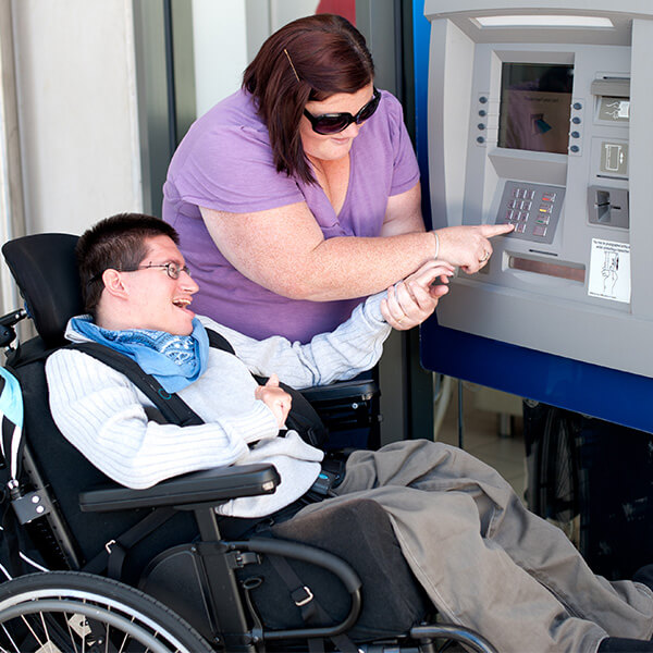 A woman teaching a man in a wheelchair how to use the ATM